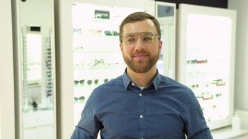 Happy young male client puts new glasses near rack and showcase with eyewear. Satisfied Customer video