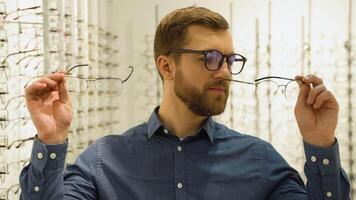 saúde Cuidado, visão e visão conceito - feliz homem escolhendo óculos às óptica loja video