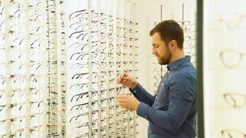 saúde Cuidado, visão e visão conceito - uma homem escolhendo óculos às óptica loja video