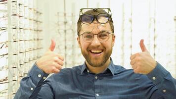 portrait de une marrant Masculin client dans nombreuses des lunettes près vitrine avec lunettes video