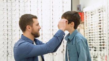 Little boy in optics store choosing glasses with his father. Ophthalmology concept video