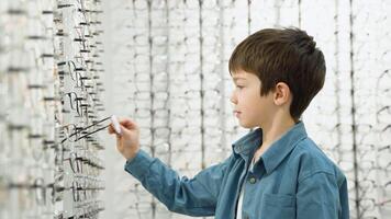 Little boy in optics store choosing glasses. Ophthalmology family concept video