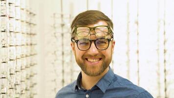portrait de une marrant Masculin client dans nombreuses des lunettes près vitrine avec lunettes video