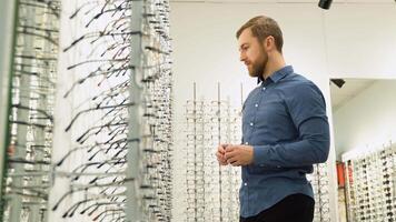 A man choosing glasses at optics store. Health care, eyesight and vision concept video