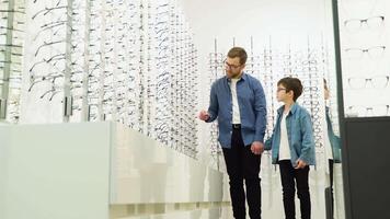 Family buy glasses. Father and son in a blue shirts choosing glasses video