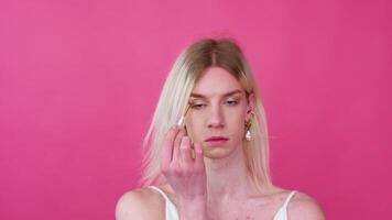 joven Transgénero hombre aplicando maquillaje en un rosado antecedentes video