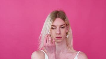 Young transgender man applying make-up on a pink background video