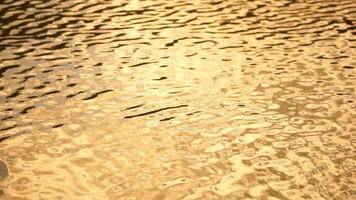 Sun reflecting on sparkling sea lake water surface, ocean at sunset, sunrise. Sunrays flickering in Ripples on water surface. Golden shimmering sea waves in sun. Slow motion. Abstract nautical nature video