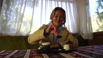 Woman pouring Turkish coffee from cezve into cup. Closeup slow motion shot of female hand with cup on square plate, on table in cafe outdoor. Traditional hot unfiltered coffee served in restaurant video