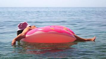 sommar semester kvinna i hatt flyter på rosa uppblåsbar munk madrass, en vatten leksak simma ringa. oigenkännlig ung kvinna avkopplande och njuter familj sommar resa högtider semester på de hav. video
