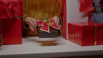 Close up of hand holding present box with ribbon and bow tie for christmas eve festivity. Woman with gifts for family preparing for holiday celebration in december. Seasonal gift video