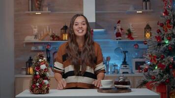 Frau reden auf Anruf im dekoriert Küche beim Zuhause zum Weihnachten Fest im Dezember. kaukasisch jung Erwachsene chatten online auf Internet mit freunde während Trinken Tee von heiß Topf video