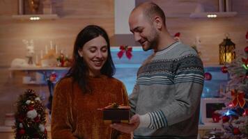 festivo donna ricevente presente a partire dal marito festeggiare Natale festa nel decorato cucina. allegro coppia con i regali baci, godendo tradizionale vacanza celebrazione. video
