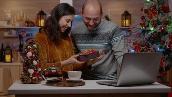 Couple celebrating christmas eve on call conference with relatives and receiving gifts in holiday decorated kitchen. Man and woman feeling cheerful for seasonal celebration video