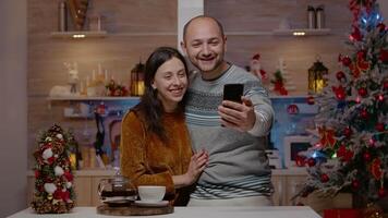 alegre Pareja utilizando llamada comunicación en teléfono inteligente hablando a familia en Navidad víspera día. hombre y mujer con remoto conversacion en en línea conferencia para fiesta temporada video