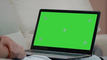 Close up of horizontal green screen on laptop. Person on couch horizontally holding gadget with chroma key screen, mockup template and isolated background. Woman with modern device video