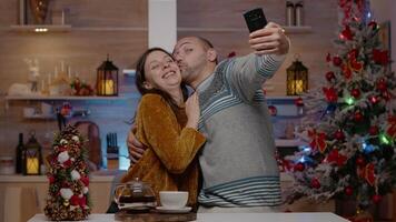 alegre Pareja tomando imágenes en Navidad víspera con teléfono inteligente casado hombre y mujer haciendo recuerdos con selfies para fiesta temporada celebracion. personas en festivo decorado cocina video