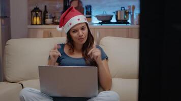 Person talking to family on call conference to celebrate christmas eve. Woman wearing santa hat while using online conference for remote holiday festivity on laptop in festive room video