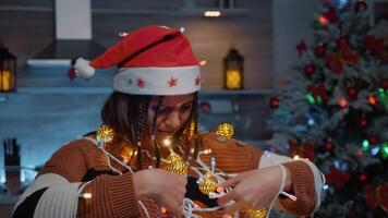 alegre mujer riendo a enredado cuerda con luces para Navidad decorando joven adulto utilizando adornos y guirnalda preparando para fiesta festividad y diciembre celebracion fiesta video