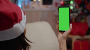 Close up of adult vertically holding smartphone with green screen. Festive woman looking at chroma key screen designed with isolated mockup template and background. Person using technology video