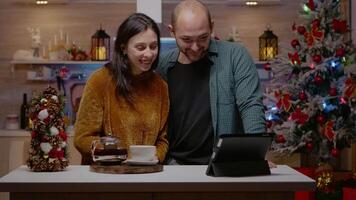 Pareja utilizando tableta para en línea llamada en Navidad víspera. hombre y mujer chateando a familia en conferencia vía Internet para fiesta temporada celebracion. festivo personas en Navidad decorado hogar video