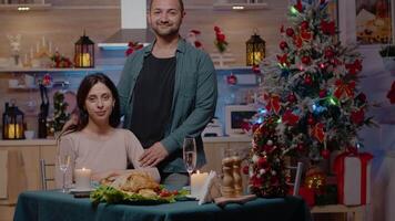 portret van paar Bij feestelijk avondeten Aan Kerstmis vooravond. Mens en vrouw op zoek Bij camera terwijl genieten van vakantie maaltijd en viering, zittend samen en gevoel vrolijk voor winter feest video