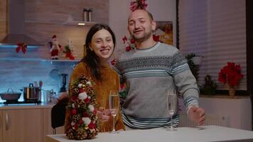 festlig par talande på ring upp konferens medan innehav glasögon av champagne för jul eve fest. människor använder sig av uppkopplad kommunikation och fira Semester med säsong- dekorationer video