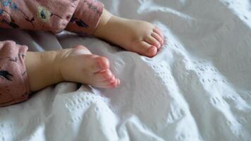 förtjusande oskyldig bebis Prova till krypande på säng den där de först tid spädbarn bebis krypa. härlig litet barn flicka ha på sig rosa bebis klänning. litet barn barn påfrestande till använda sig av ben för lyft ben och kropp. stänga upp ben video