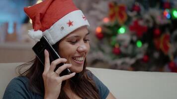 stänga upp av glad kvinna använder sig av smartphone till ring upp familj på jul eve. person bär santa hatt och talande till släktingar på telefon till fira Semester avlägset. vuxen chattar video