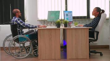 Businesswoman talking with paralysed colleague analyzing financial statistics, looking at desktop and typing. Disabled, immobilized freelancer working in corporate company using modern technology. video