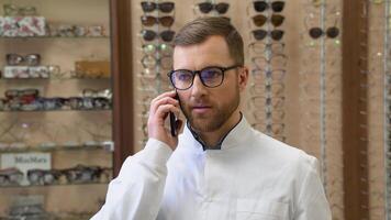 Confident doctor advises a patient by phone in optics. Optician selling glasses video