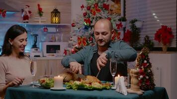 Couple eating chicken at festive dinner on christmas eve celebrating with traditional food and glasses on champagne at home. Man and woman enjoying holiday festivity with food and alcohol video