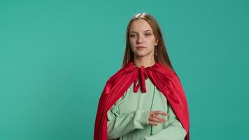 Smiling teenager portraying superhero wearing red cape, isolated over studio background. Portrait of cheerful heroic person posing as hero in costume with mantle, camera A video