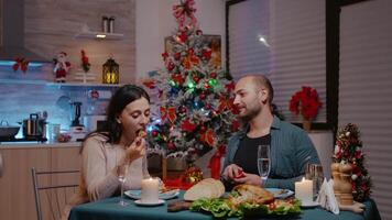 Man proposing with engagement ring to woman at festive dinner. Couple getting engaged while celebrating christmas eve with chicken meal and glasses of champagne. Cheerful people in love video