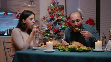 casal tilintar óculos do champanhe às Natal jantar. festivo homem e mulher comendo frango refeição e bebendo álcool para feriado celebração. pessoas desfrutando tradicional festividade video