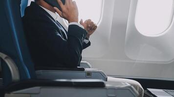 bem sucedido ásia homem de negocios dentro terno e óculos senta dentro privado jato e usa Smartphone, coreano empreendedor moscas dentro a avião e tipos em a telefone conectados video