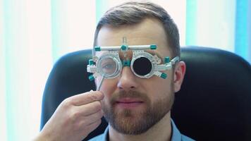 A handsome male patient wearing special ophthalmic glasses. Doctor checks vision to the patient video