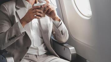 bem sucedido ásia homem de negocios dentro terno e óculos senta dentro privado jato e usa Smartphone, coreano empreendedor moscas dentro a avião e tipos em a telefone conectados video