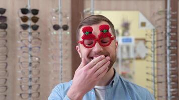 een grappig Mens in rood carnaval nieuw jaar bril gaapt in optiek winkel video