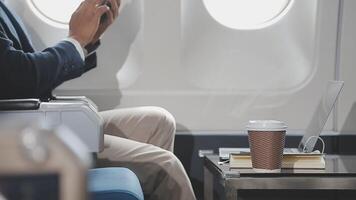 riuscito asiatico uomo d'affari nel completo da uomo e bicchieri si siede nel privato Jet e usi smartphone, coreano imprenditore mosche nel un aereo e tipi su il Telefono in linea video