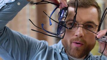 Excited surprised man holds many new glasses in his hands at optical shop. Choosing glasses concept video