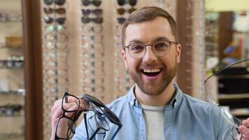 Excited surprised man holds many new glasses in his hands at optical shop. Choosing glasses concept video