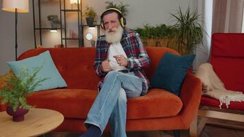 Happy relaxed man in wireless headphones dancing listening favorite rock n roll music on home couch video