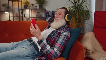 Happy relaxed man in wireless headphones dancing listening favorite rock n roll music on home couch video