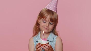 Happy child girl kid celebrating birthday party, makes wish blowing burning candle on small cupcake video