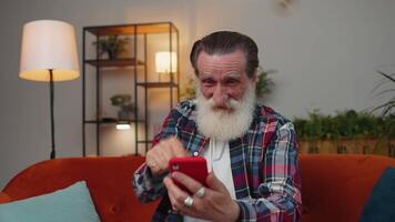 mayor abuelo a hogar sofá utilizar teléfono inteligente celebrar genial grande lotería ganar bote, bueno Noticias video