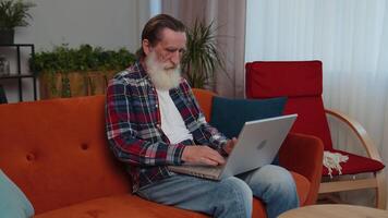 Senior avô homem trabalhador autonomo trabalhando em computador portátil, envia mensagens, faz conectados compras às casa video