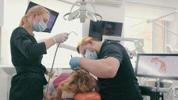 Zahnarzt und seine Assistent im schützend Masken behandeln ein Patienten Zähne im ein Dental Klinik. Gesundheitswesen und Medizin Konzept. modern Dental Klinik video