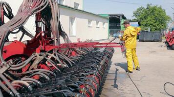 Washing of large-sized agricultural machinery. Cleaning the seeder after work in the field. A worker washes an agricultural machine with water under pressure. video