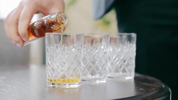 fermer de une homme verser whisky dans une verre. sur le table sont Trois verre des lunettes dans lequel whisky est versé video